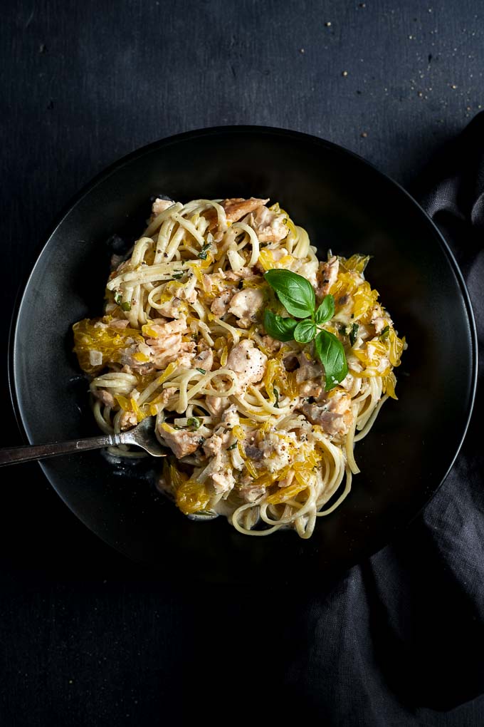 bowl of ceamy salmon pasta garnished with basil and orange pieces