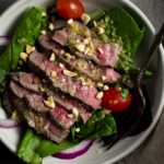 thai beef salad in a bowl with tomatoes and red onions