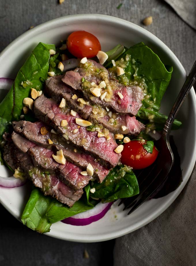 thai beef salad in a bowl with tomatoes and red onions