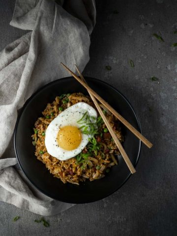 bowl of fried rice topped with an egg and sliced green onions with chopsticks