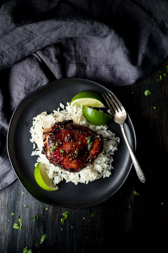 roasted chicken thigh on rice with 2 limes on a plate with a fork