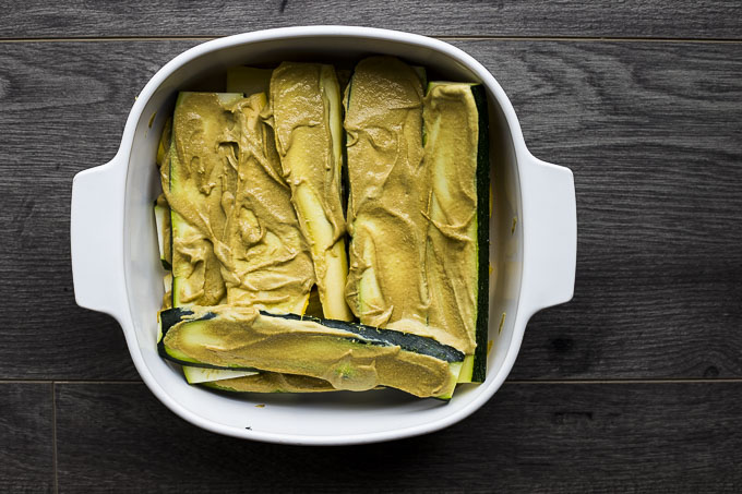sliced of raw squash covered in mustard in a baking dish