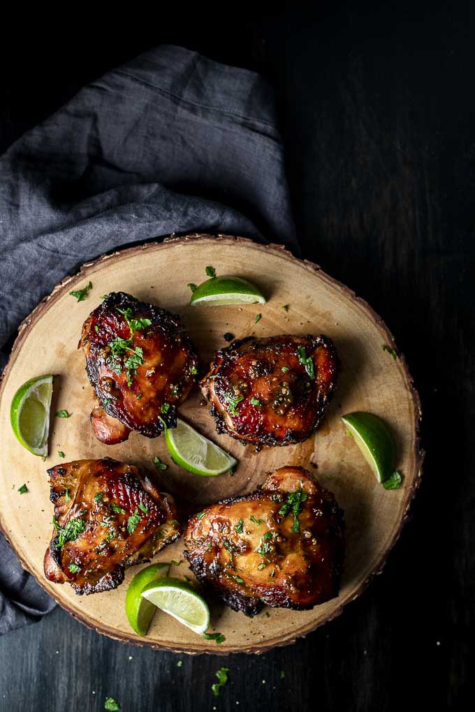4 roasted chicken thighs on a wooden board with cilantro and limes