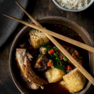 ribs, tofu, mushroom, chilies and green onions in broth with chopsticks