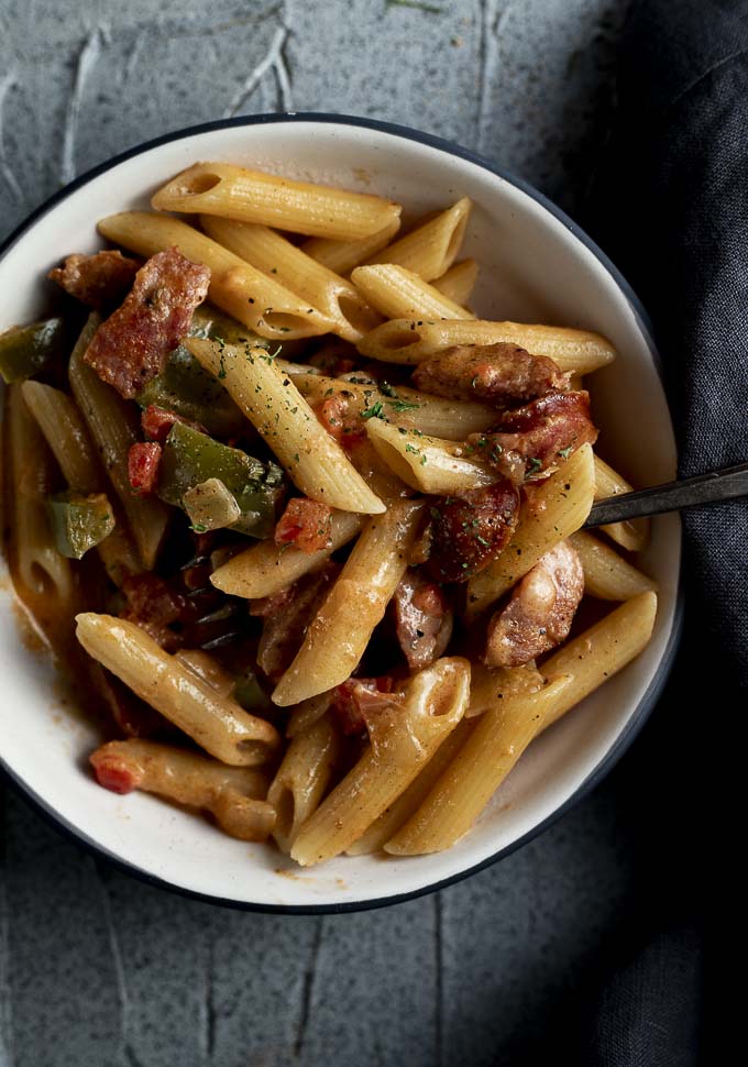 bowl of pasta with peppers, onions and sausage in a cream sauce