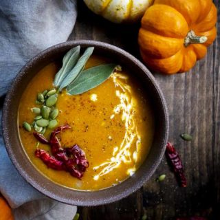 bowl of orange soup with pumpkin seeds, chilies and sage