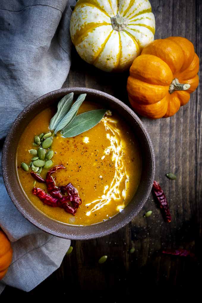 bowl of orange soup with pumpkin seeds, chilies and sage