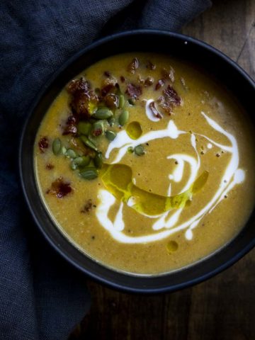 bowl of orange soup with cream and pumpkin seeds