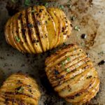 hasselback potatoes garnished with parsley on a baking sheet