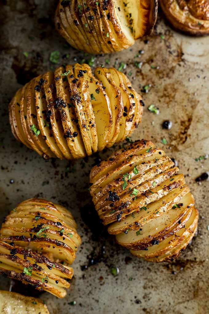 hasselback potatoes garnished with parsley on a baking sheet