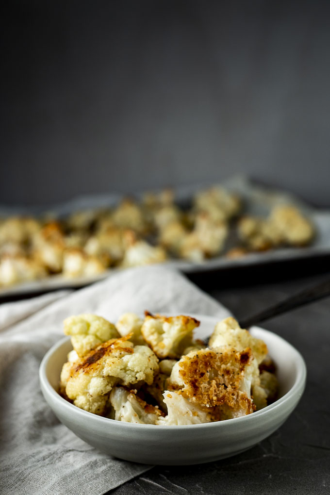 bowl of roasted cauliflower with tray of cauliflower in the background