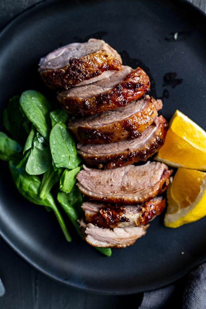 sliced roasted duck breast on a plate with greens and orange slices