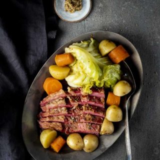 a plate of corned beef and cabbge with potatoes and carrots and mustard on the side