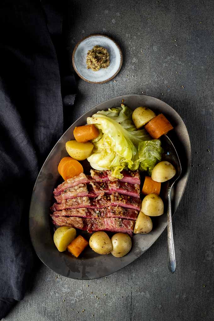 a plate of corned beef and cabbge with potatoes and carrots and mustard on the side