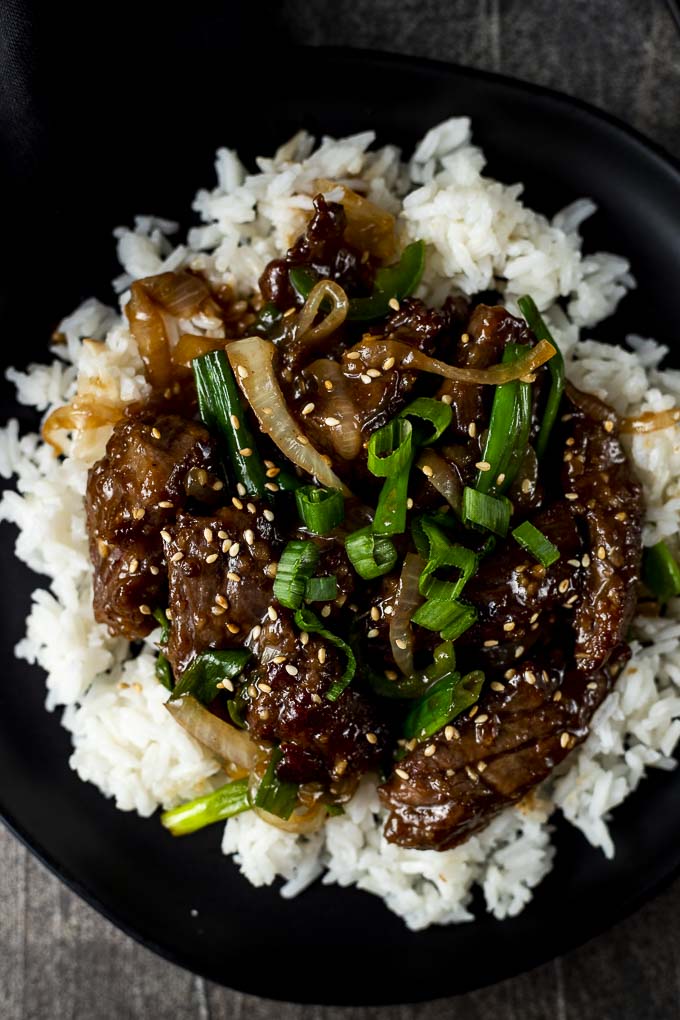 mongolian beef on a plate over rice with sesame seeds