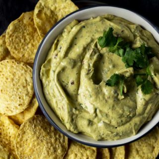 a bowl of avocado dip with chips on the side