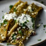 2 enchiladas on a plate with sour cream and cilantro