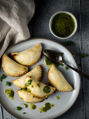 a plate of vegetarian empanadas drizzled with green chimichurri sauce