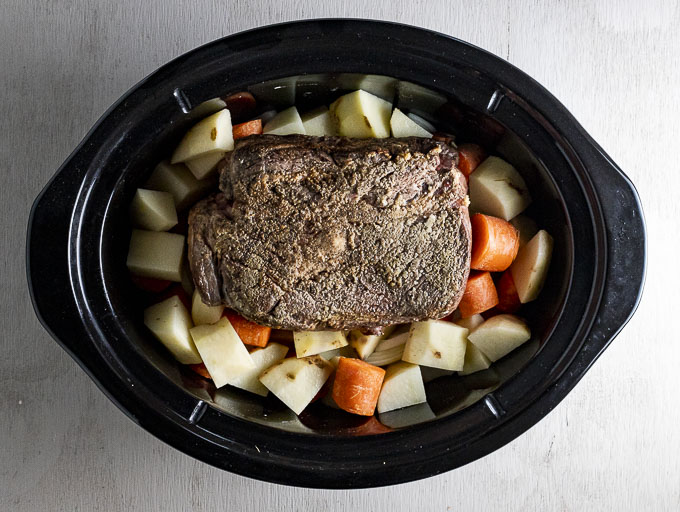 potatoes and carrots in a slow cooker with browned beef roast on top