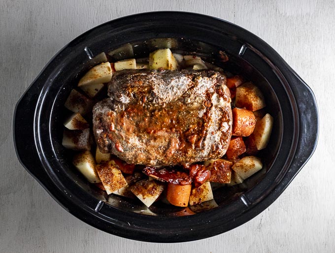 beef roast on top of potatoes and carrots in a slow cooker