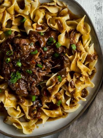 braised beef over egg noodles with green onions