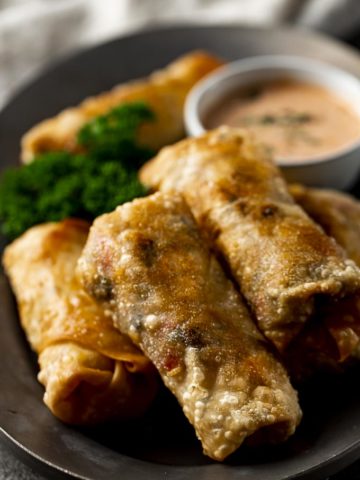 plate of fried egg rolls with orange sauce and pasrley
