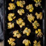 crispy baked smashed potatoes garnished with parsley on a tray