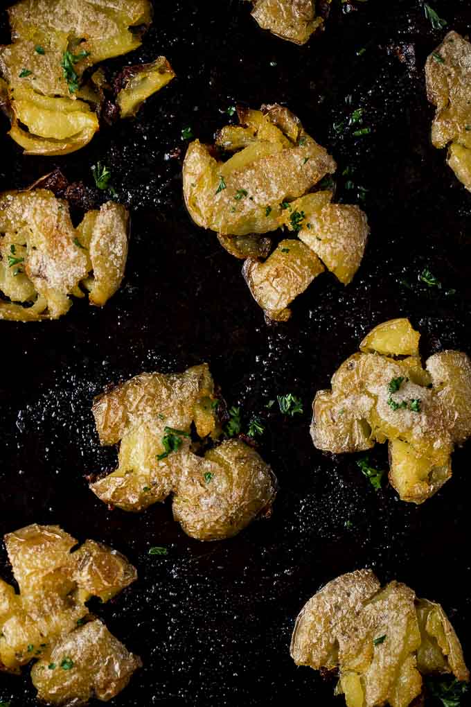 smashed potatoes on a tray with seasoning and parsley - roasted