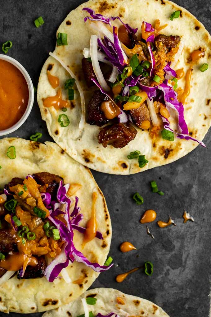 tacos laid flat on a platter with cabbage, orange sauce and green onions