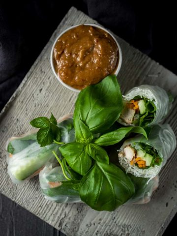 summer rolls with chicken and vegetables on a plate with herbs and dipping sauce