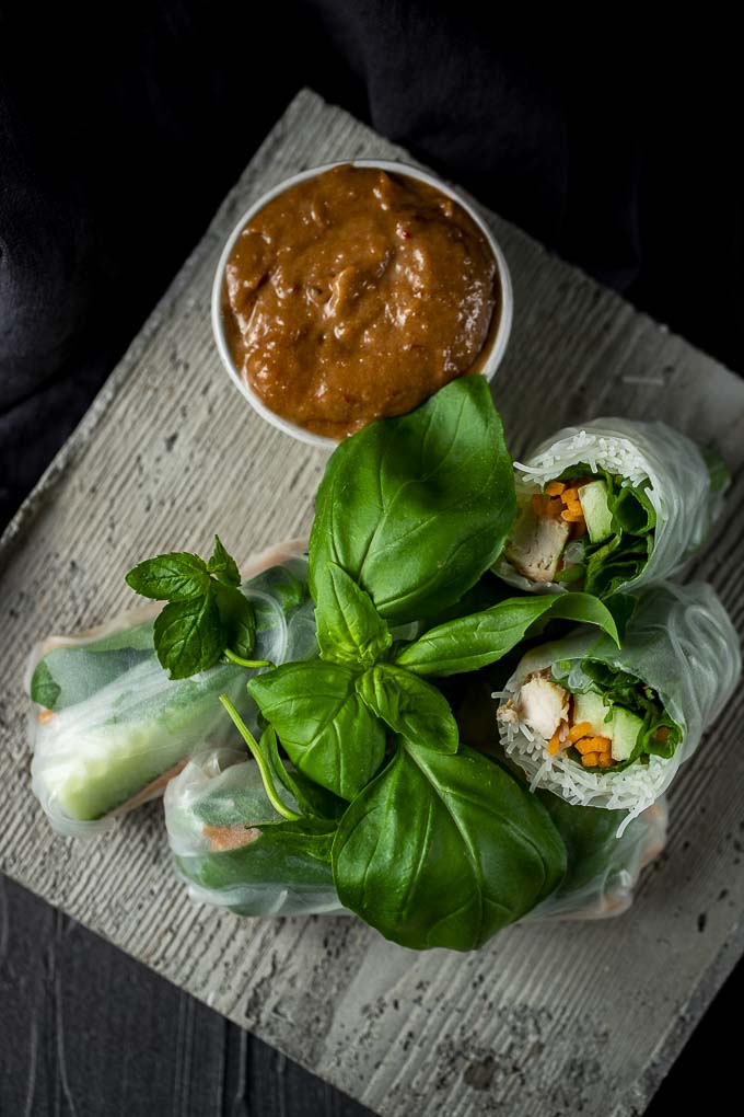 summer rolls with chicken and vegetables on a plate with herbs and dipping sauce