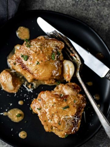 2 chicken thighs on a plate with garlic clovesand silverware
