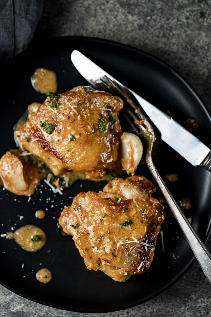 2 chicken thighs on a plate with garlic clovesand silverware 