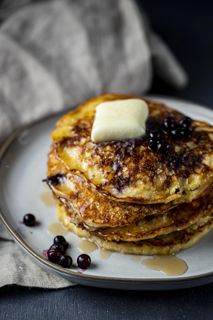 blueberry pancakes on a plate with blueberries on top.
