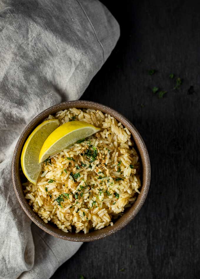 bowl of yellow rice garnished with parsley and limes
