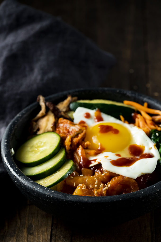 rice bowl topped with egg, cucumber, veggies and kimchi, drizzled in a red sauce