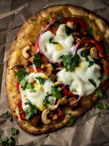 naan pizza with melted cheese, red pepper, cilantro, cashews and yellow sauce