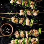 yakitori on a platter with sauce bowls and sesame seeds