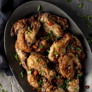 plate of fried chicken wings sprinkled with cilantro and red chilies