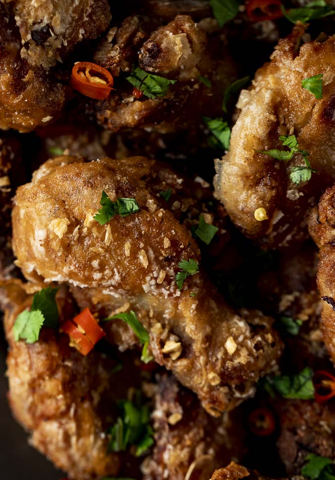 close up photo of a fried chicken wing with green hers and red chilies