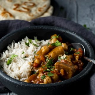 a bowl of curry with a spoon and naan bread on the side