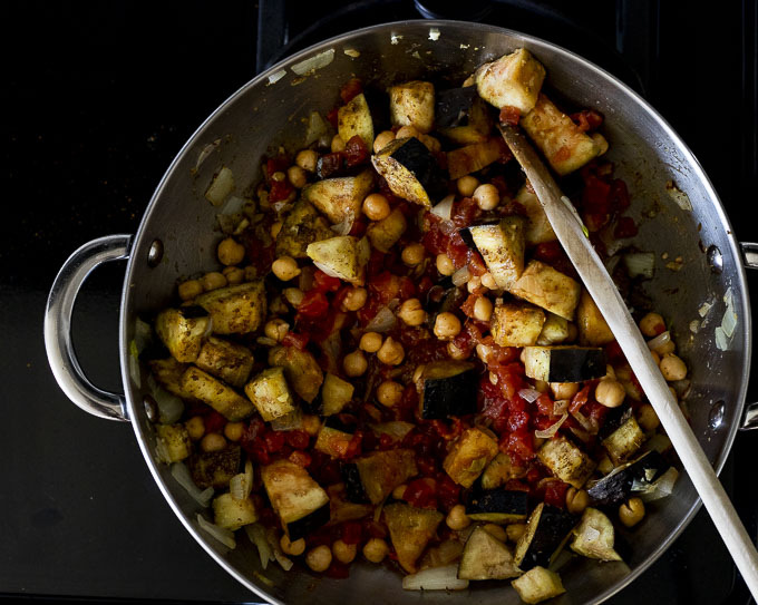 eggplant, chickpeas and tomatoes being cooked in a skillet