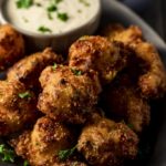 fried hushpuppies in a pile with sauce in the background