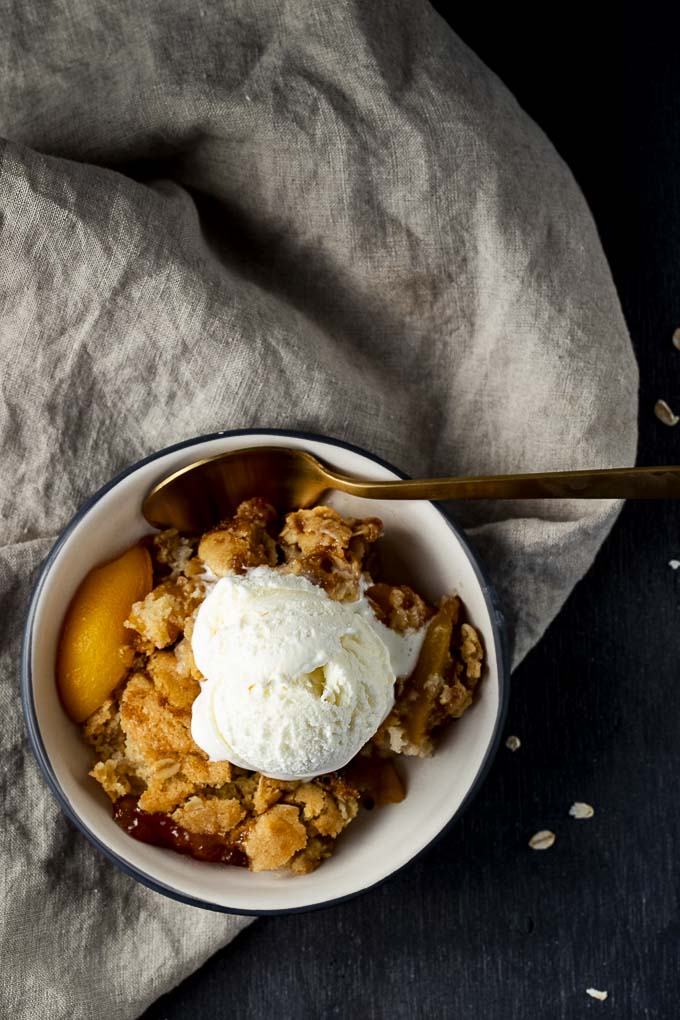bowl of peach cobbler with a spoon and scoop of ice cream