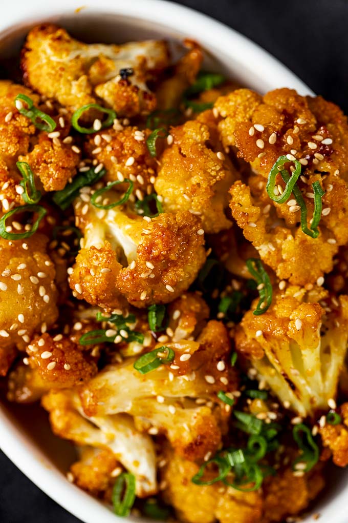 close up photo of cauliflower in orange sauce with sesame seeds and green onions