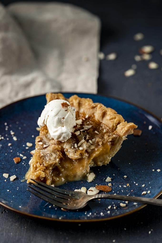 piece of almond tart on a plate with crushed almonds and ice cream