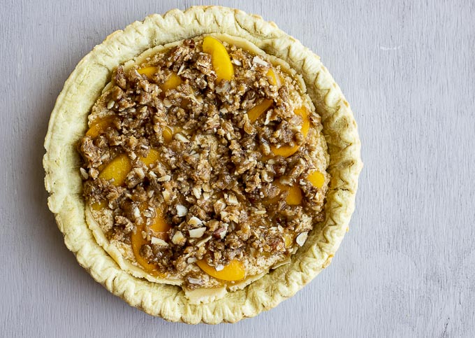 unbaked pie topped with peaches and struesel topping