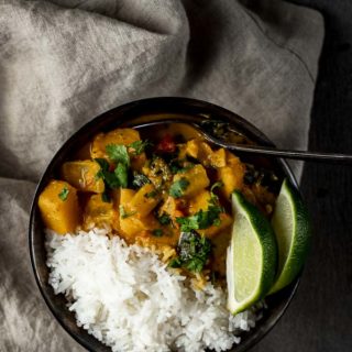 a bowl of orange butternut squash curry with rice and sliced limes