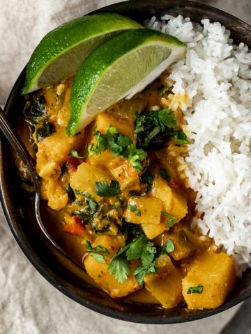 orange colored butternut squash curry in a bowl with rice and fresh lime slices