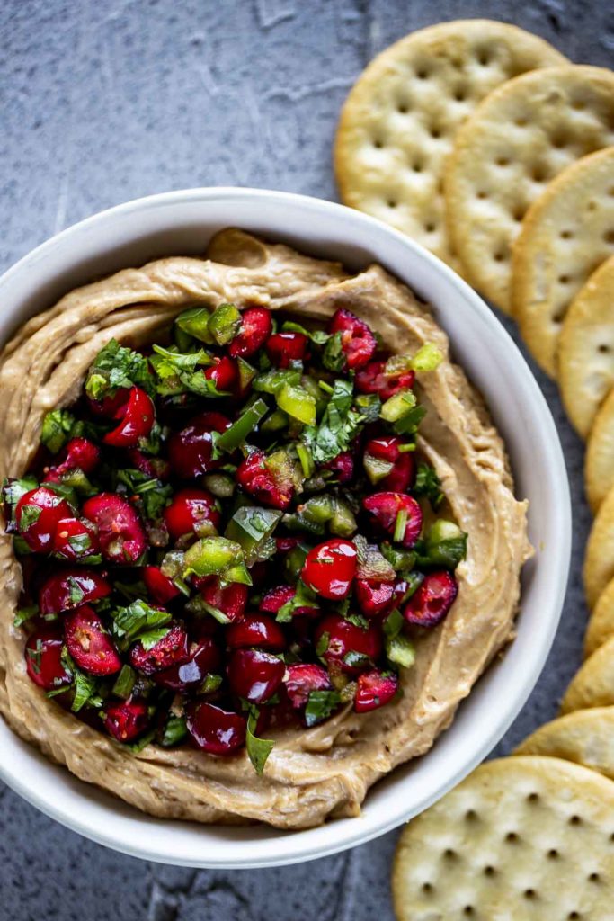 diced jalapenos and cranberries with cilantro over a cream colored dip with crackers on the side
